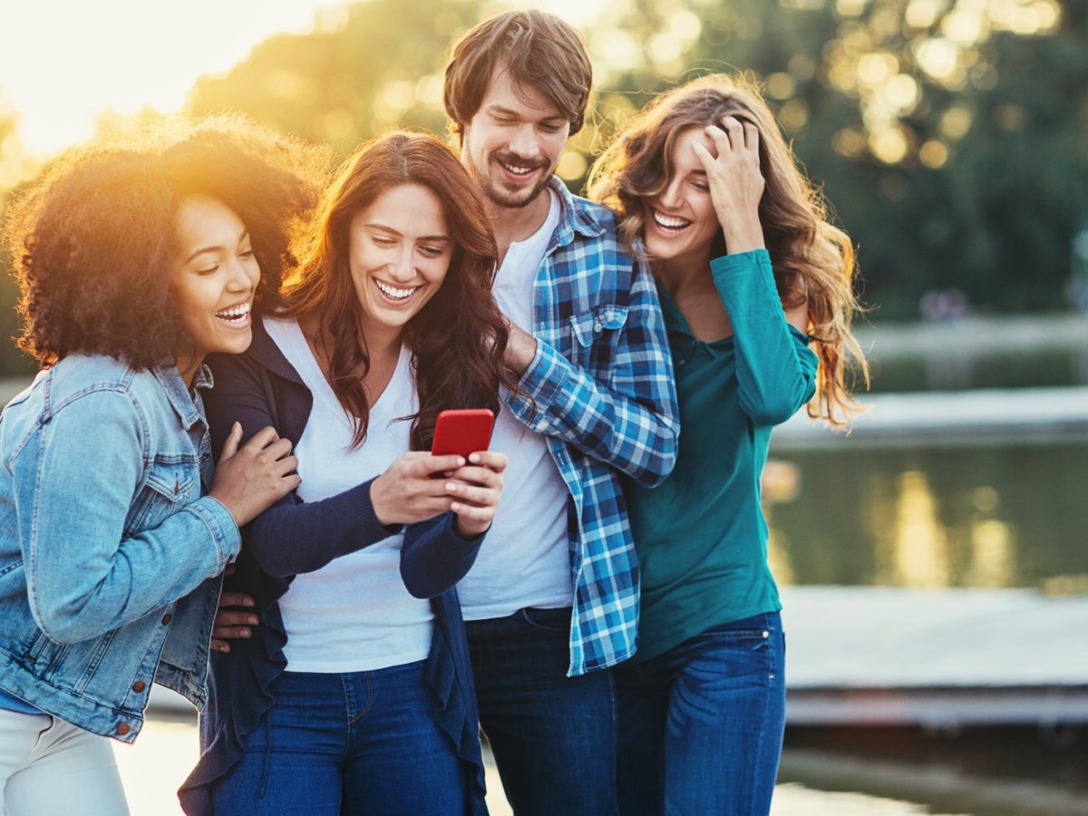 Eine Gruppe Menschen schaut lachend auf ein Smartphone.