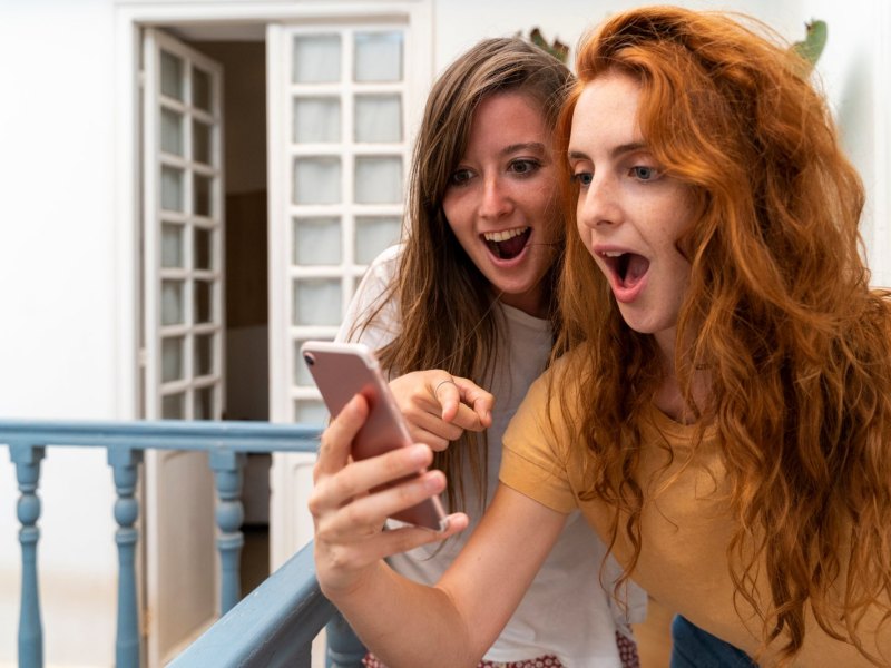 Zwei Frauen schauen überrascht auf ein Handy.