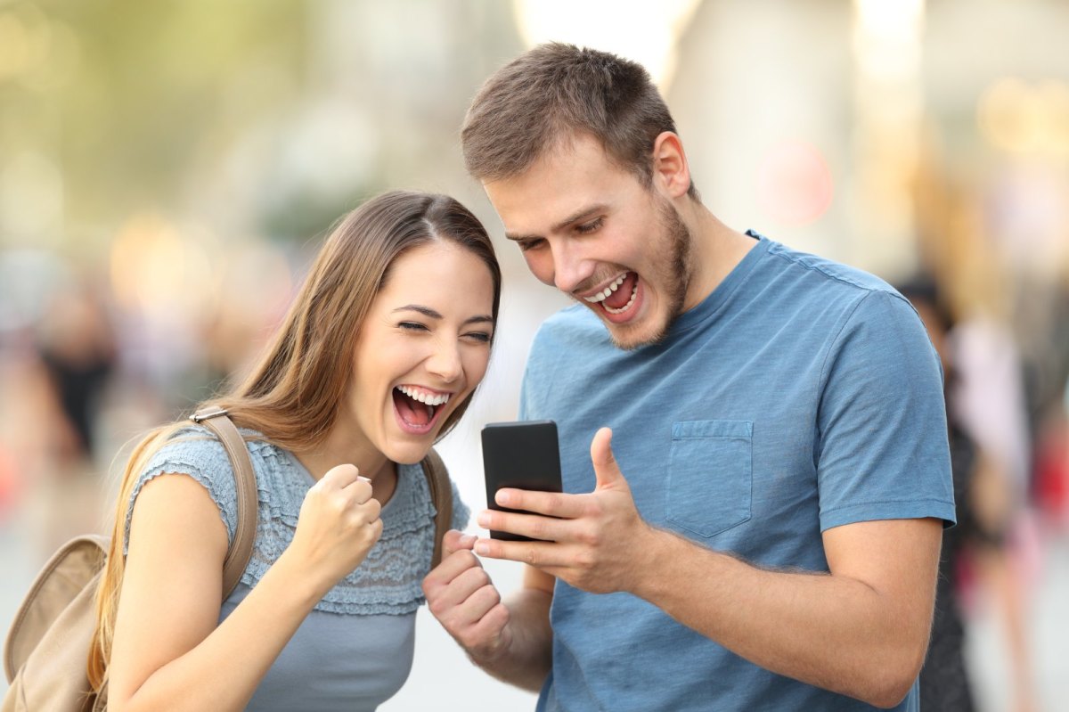 Frau und Mann freuen sich und schauen dabei auf ein Handy.