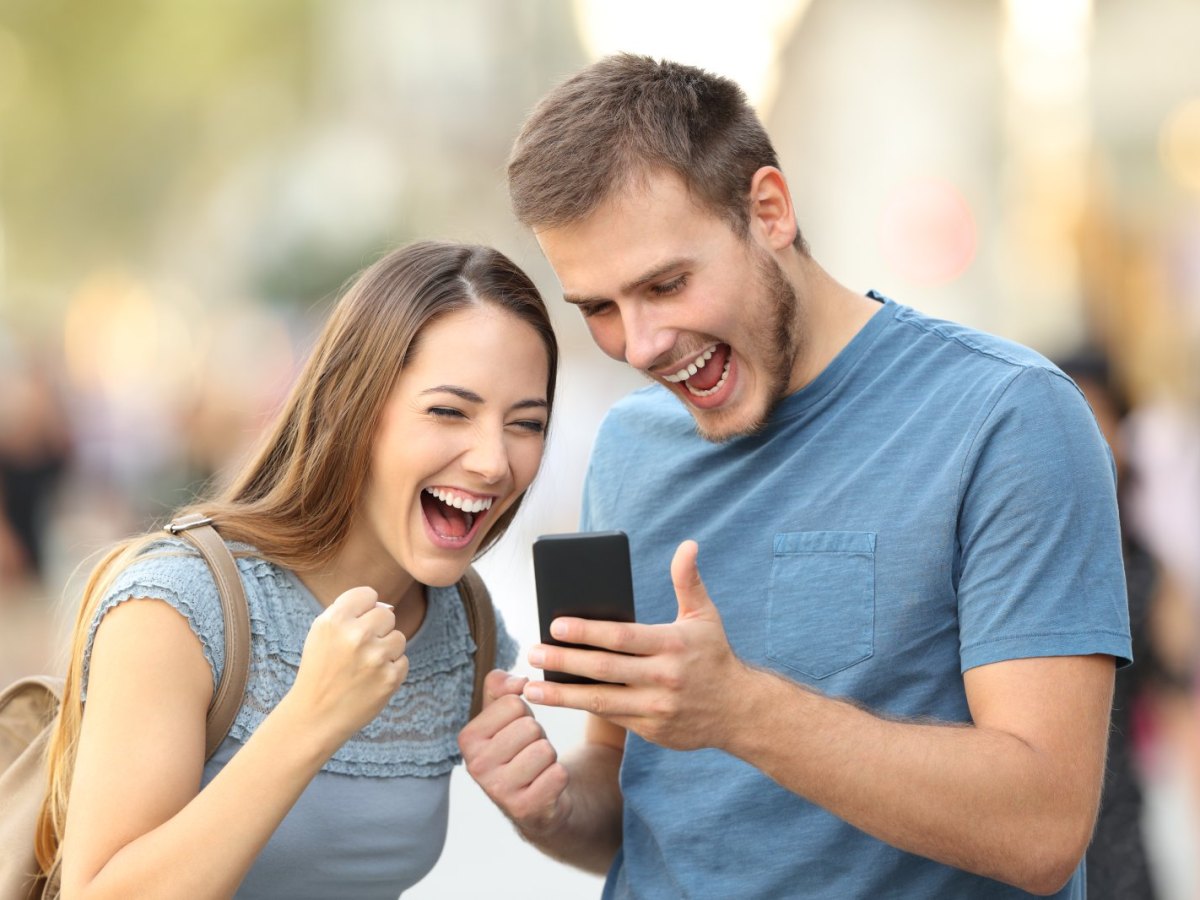 Frau und Mann freuen sich und schauen dabei auf ein Handy.