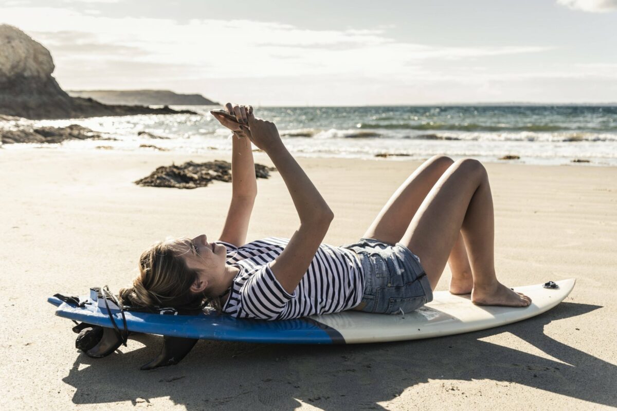 Frau liegt auf Surfbrett am Strand.