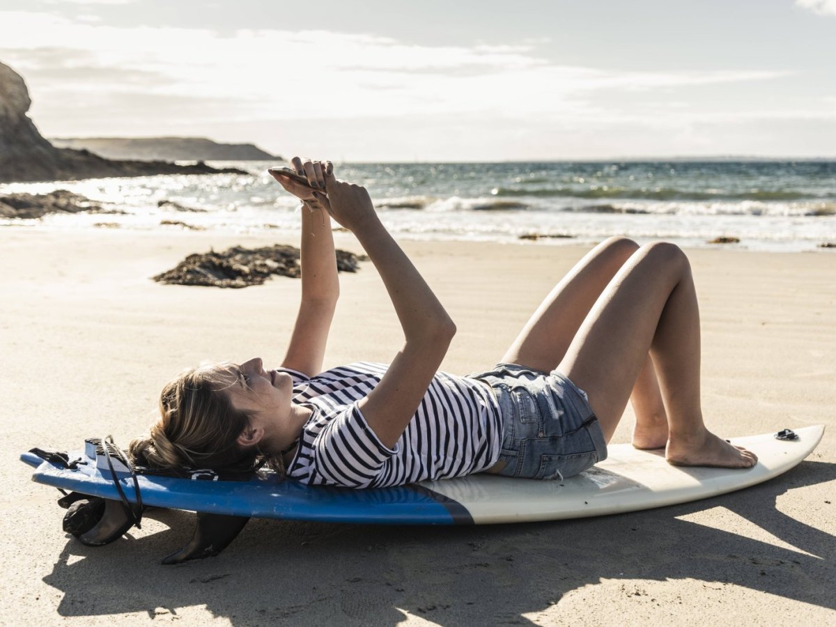 Frau liegt auf Surfbrett am Strand.