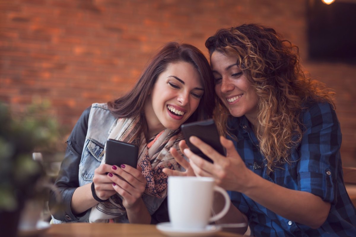 Zwei Frauen sitzen im Cafe und vergleichen Handys.