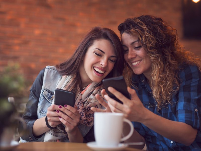Zwei Frauen sitzen im Cafe und vergleichen Handys.