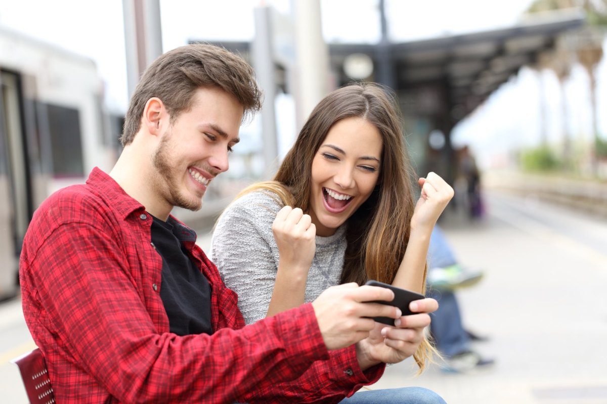 Zwei junge Leute freuen sich und schauen auf ein Handy.