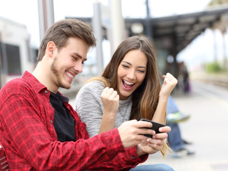 Zwei junge Leute freuen sich und schauen auf ein Handy.