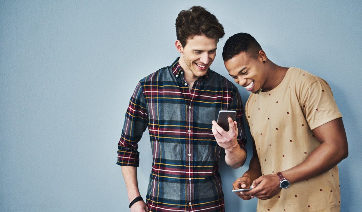 Zwei junge Männer schauen fröhlich auf ihre Handys.