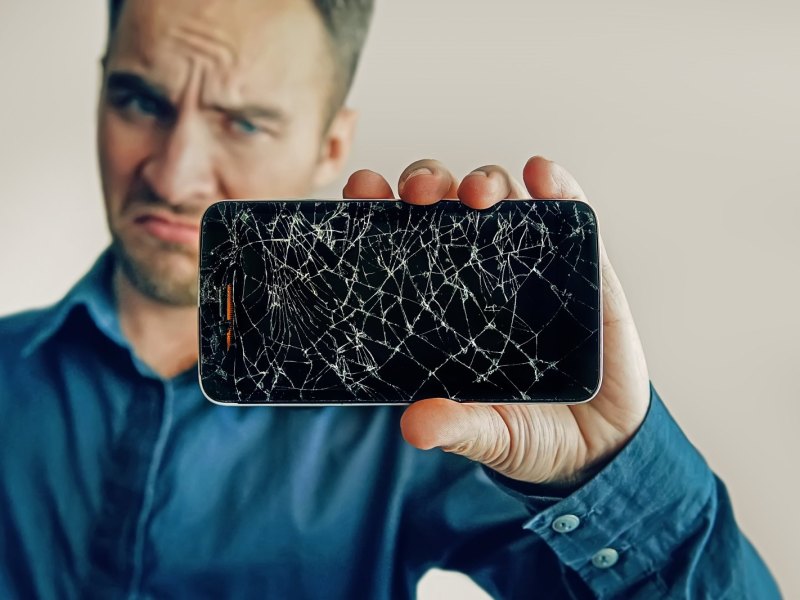 Mann hält ein Handy mit gebrochenem Display in der Hand
