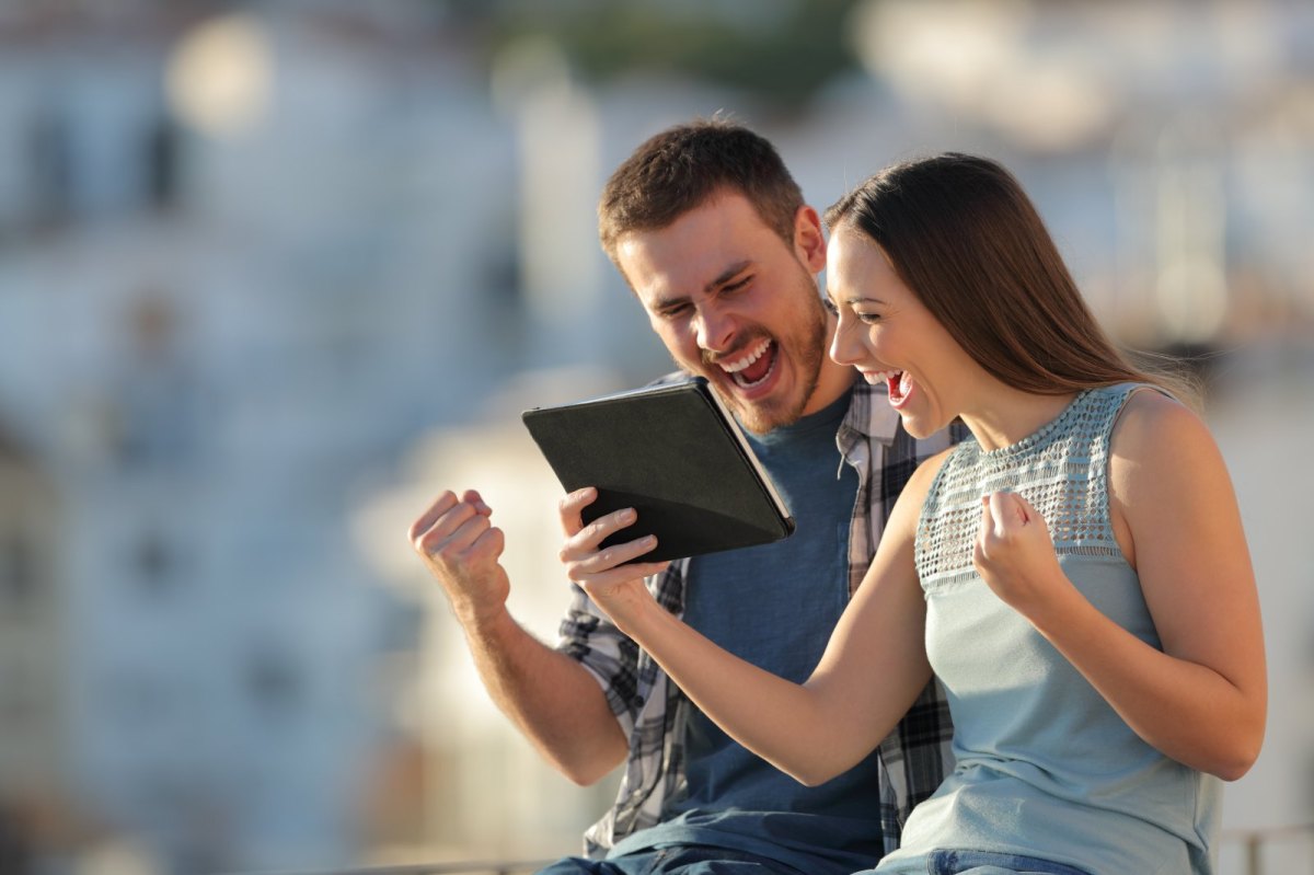 Eine Frau und ein Mann nutzen fröhlich ein iPad.
