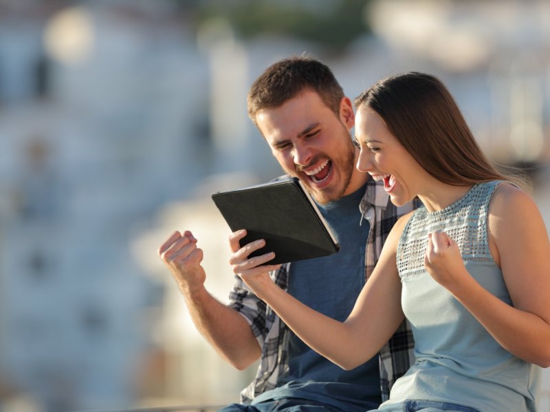 Eine Frau und ein Mann nutzen fröhlich ein iPad.