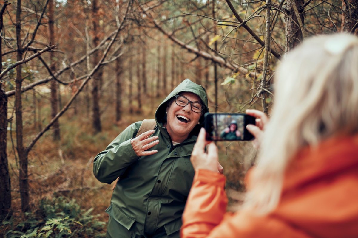 Frau nimmt Handyfoto in Herbstwald auf