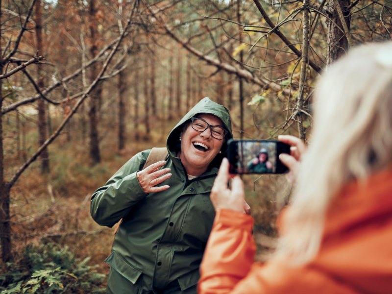 Frau nimmt Handyfoto in Herbstwald auf