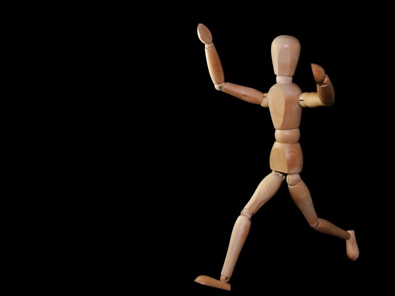 Eine Holzfigur in Menschengestalt wird im Laufen dargestellt.