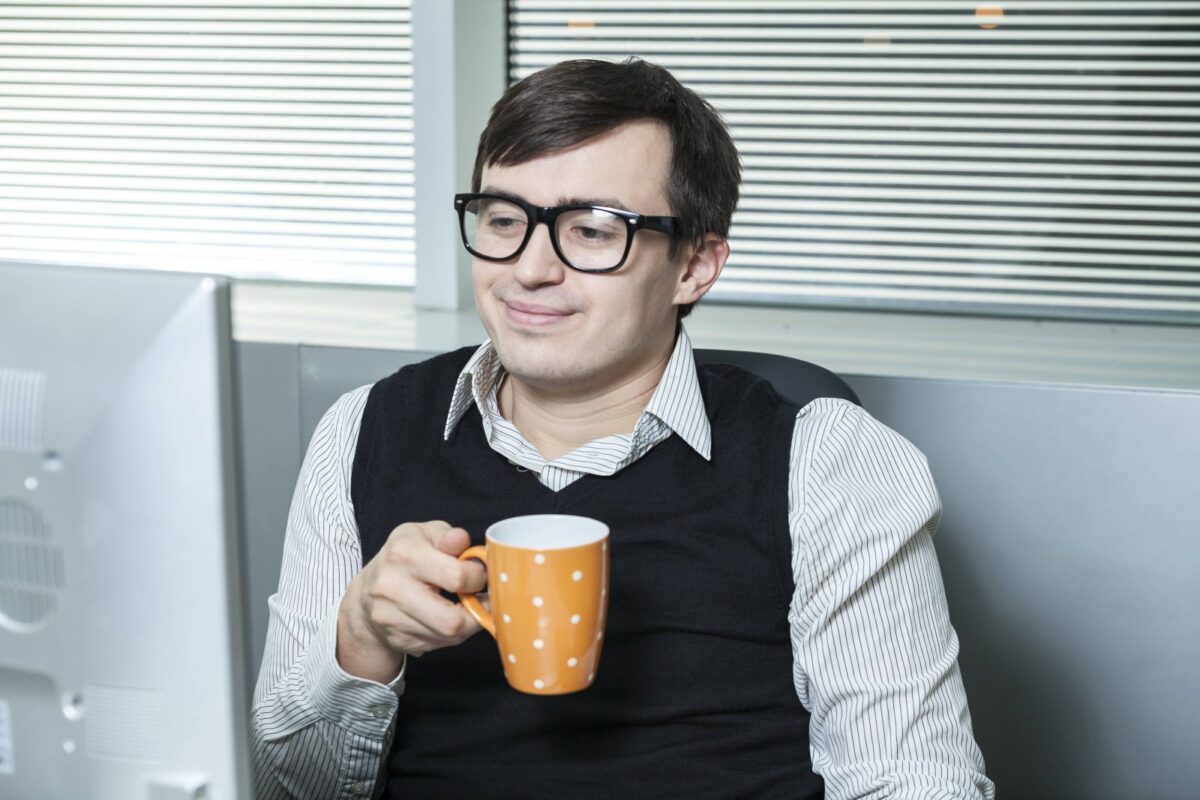 Ein Mann schaut auf seinen Monitor und trinkt Kaffee .