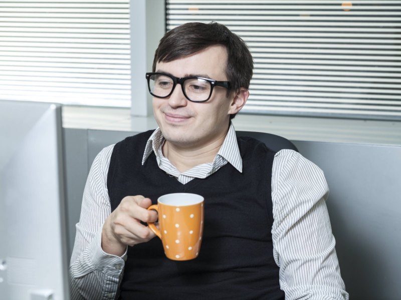 Ein Mann schaut auf seinen Monitor und trinkt Kaffee .