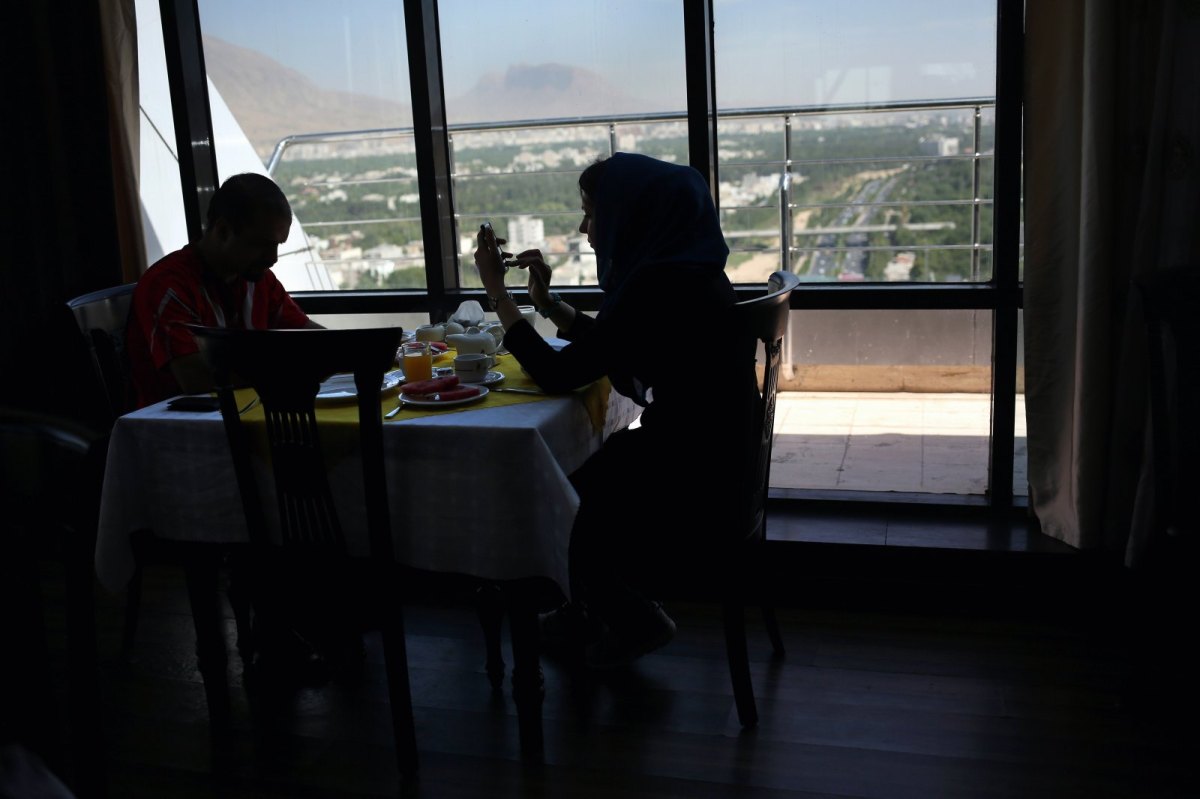 Eine Frau im Iran checkt ihr Smartphone am Frühstückstisch.