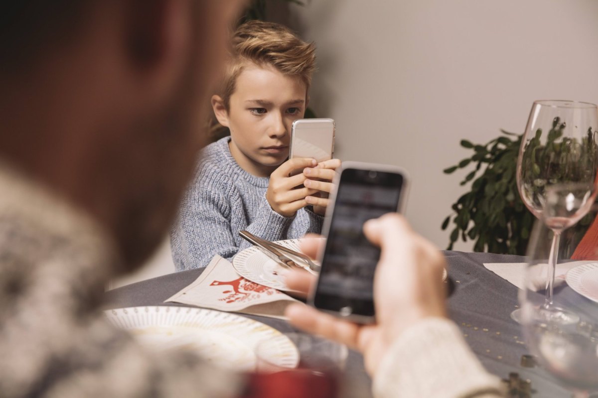 Ein Junge sitzt mit seinem Smartphone am Abendbrottisch