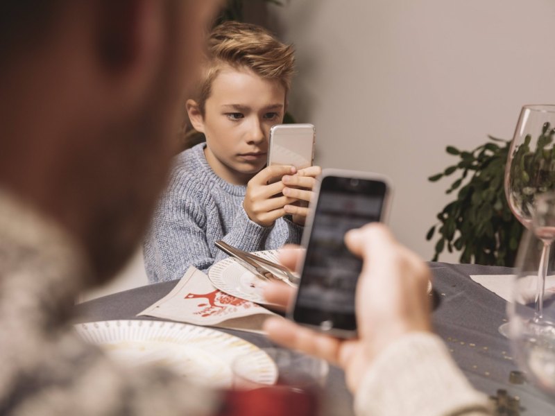 Ein Junge sitzt mit seinem Smartphone am Abendbrottisch