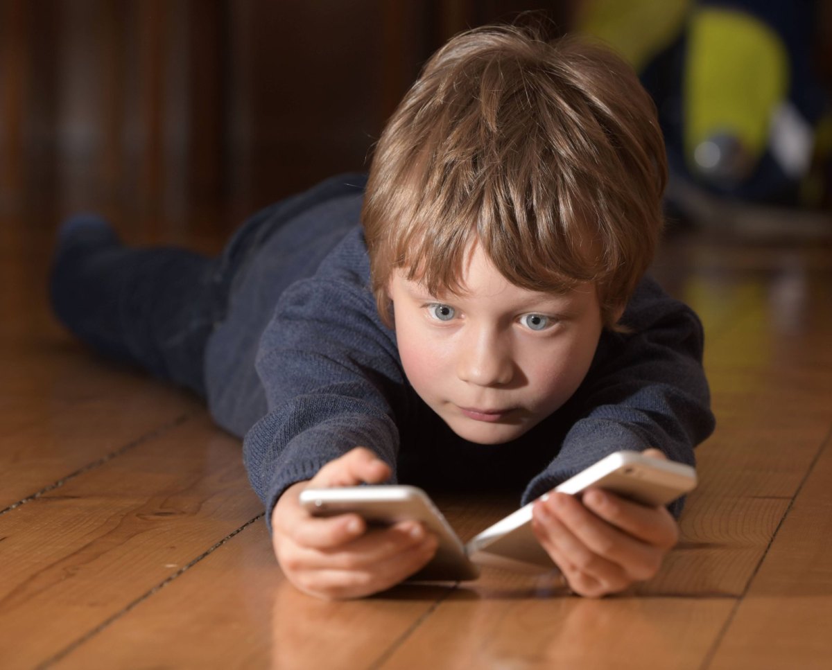 Junge liegt auf dem Boden und hält zwei Smartphones in der Hand