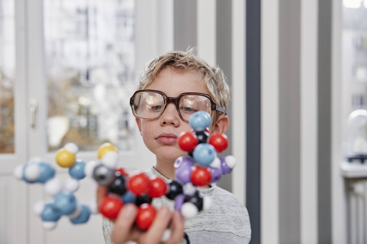 Junge mit zu großer Brille hält Molekül-Modell in der Hand