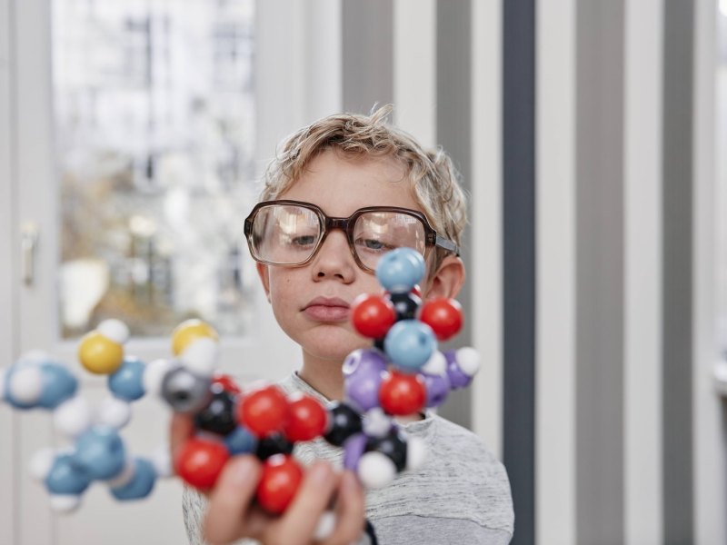 Junge mit zu großer Brille hält Molekül-Modell in der Hand