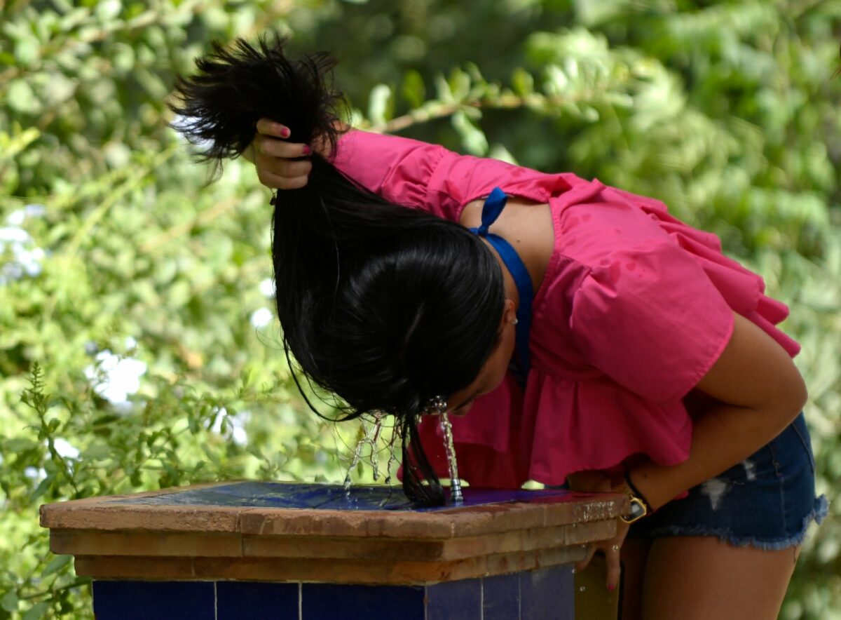 Frau kühlt sich Kopf in einer Wasserfontäne.