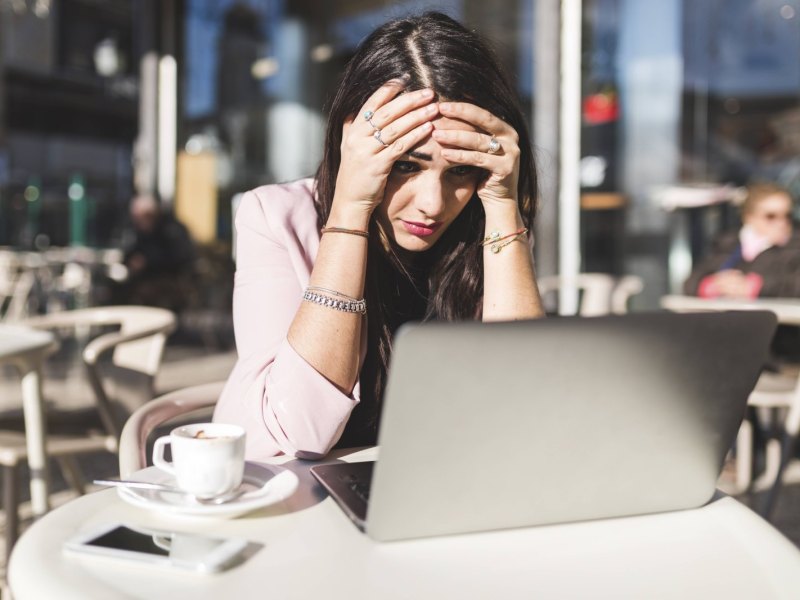 Frau schlägt geschockt über ihrem Laptop die Hände zusammen.