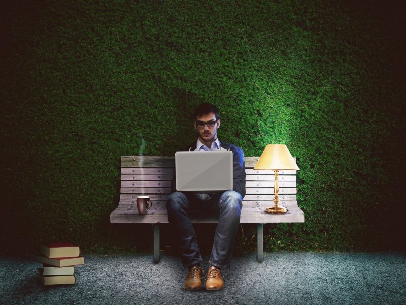 Ein Mann sitzt im Garten auf einer Bank und benutzt einen Laptop