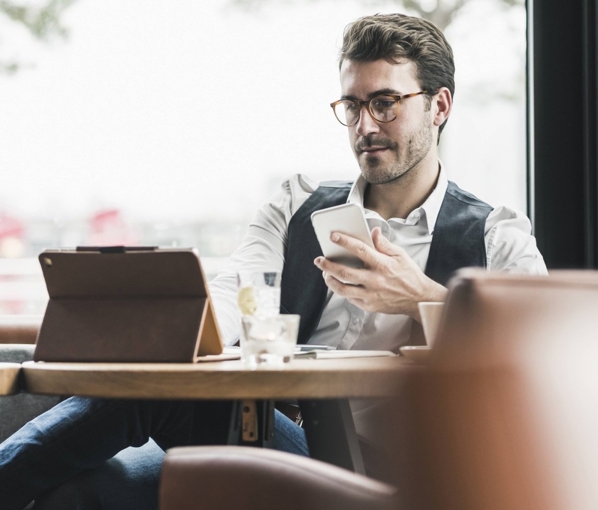 Mann am Tablet mit Smartphone in einem Café
