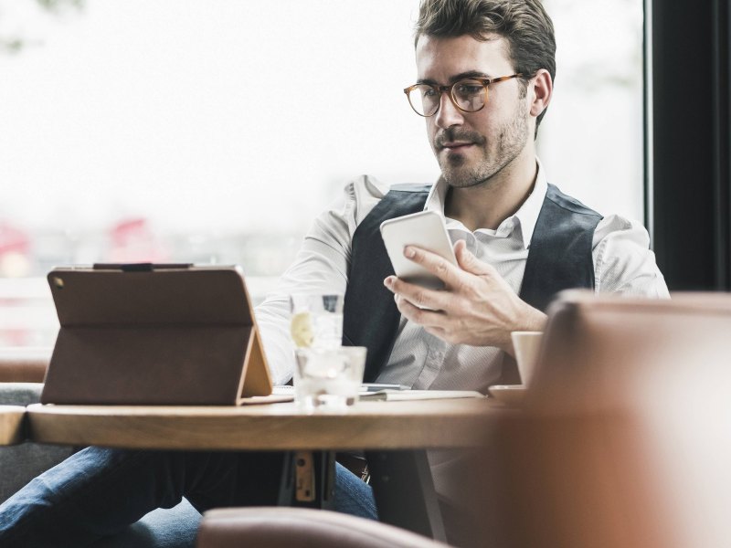 Mann am Tablet mit Smartphone in einem Café