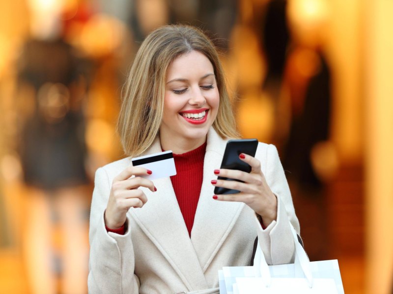 Frau mit Handy und Kreditkarte in der Hand.