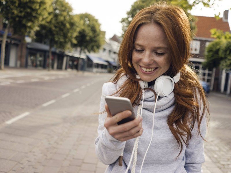 Eine Frau hört mit Kopfhörern auf ihrem Smartphone Musik.