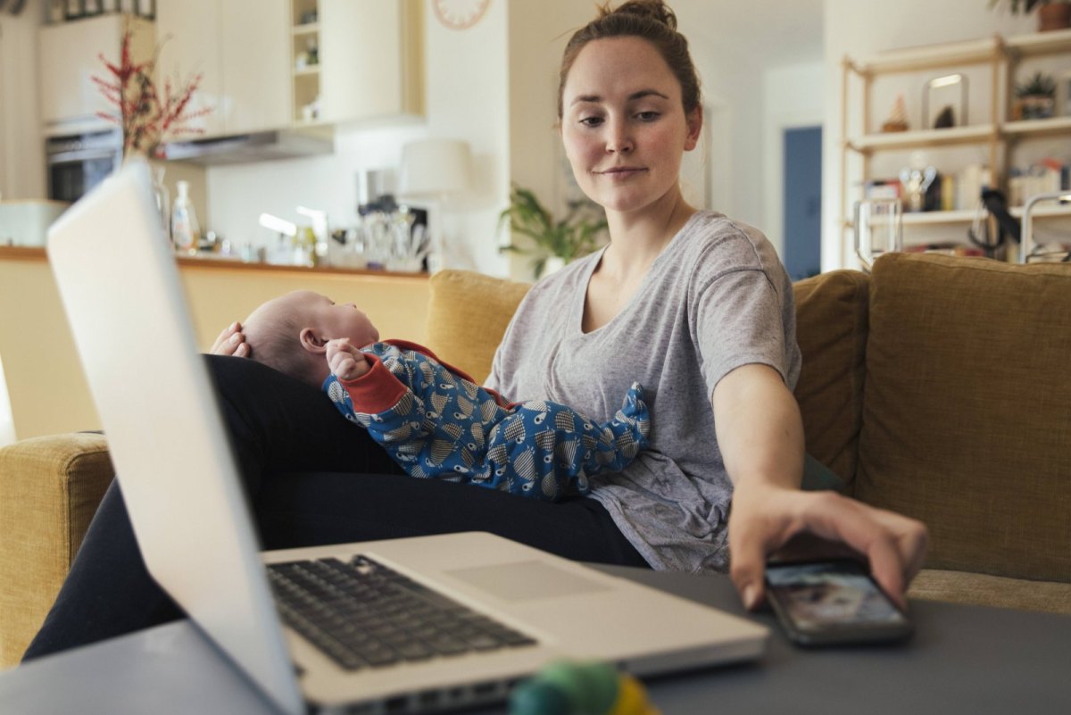 Frau mit Baby auf dem Schoss greift nach Smartphone