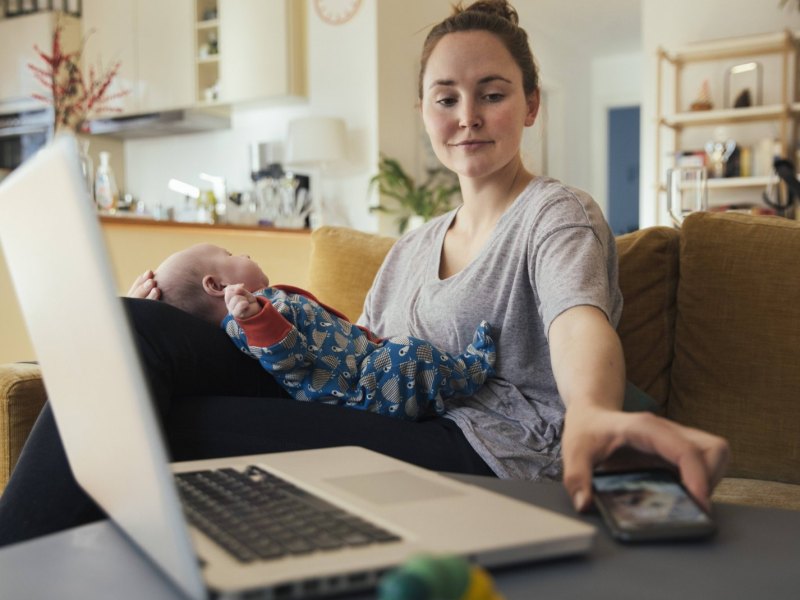 Frau mit Baby auf dem Schoss greift nach Smartphone