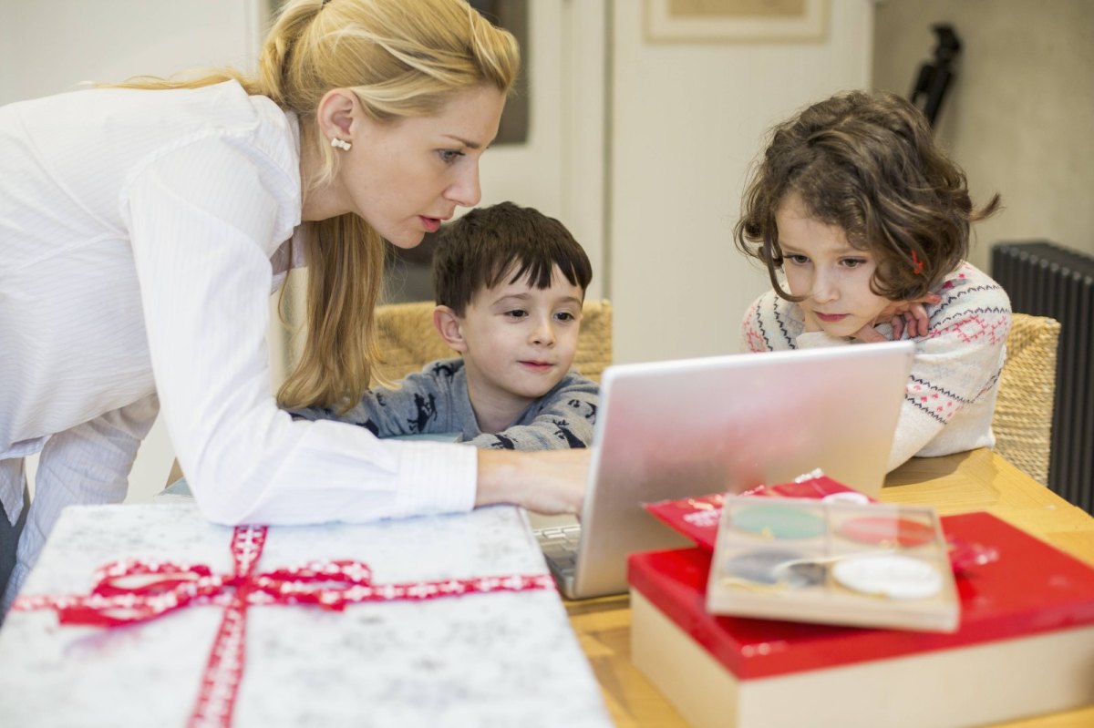 Eine Mutter schaut mit ihren Kinder am Küchentisch auf einen Laptop.