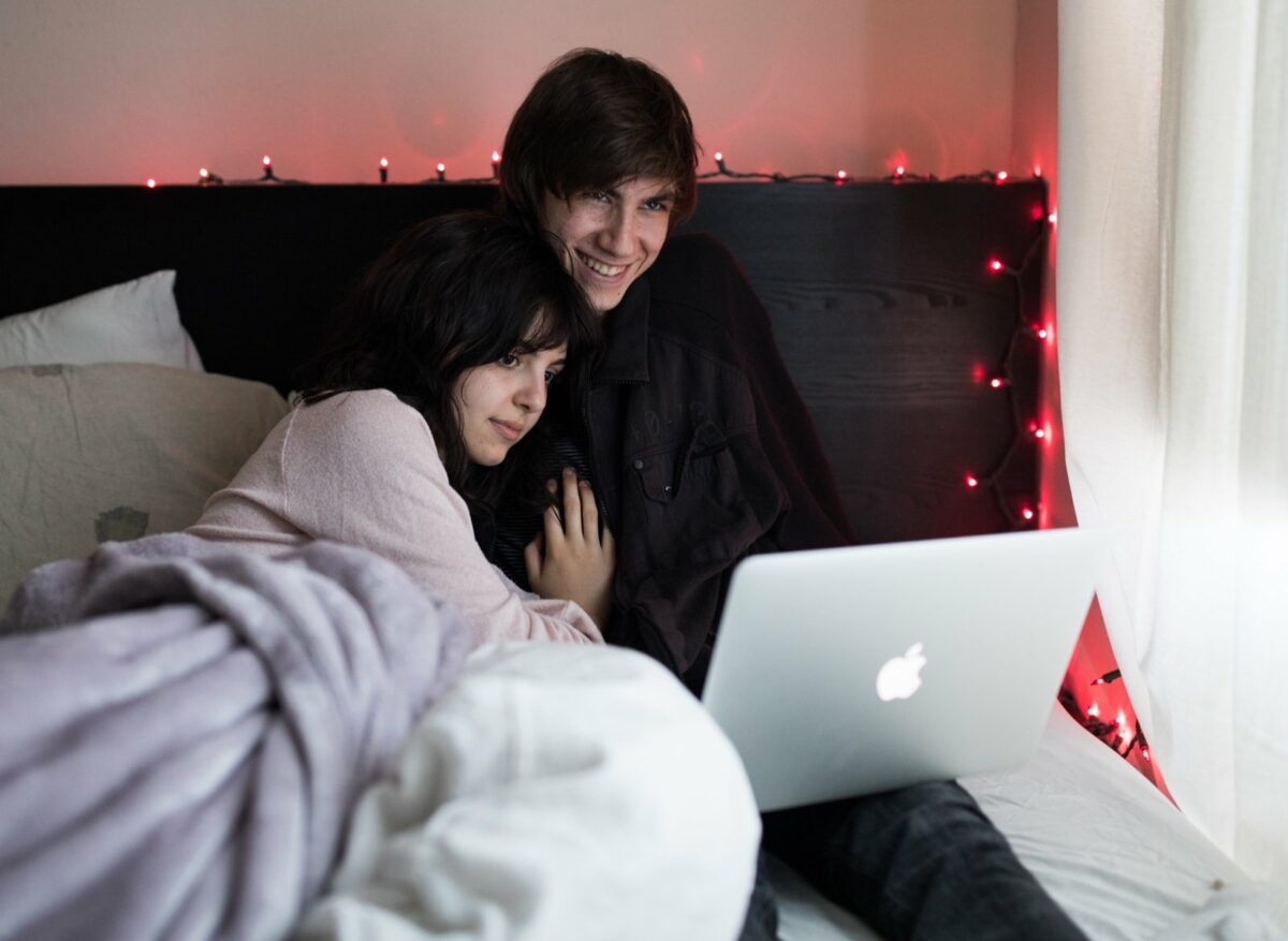 Paar liegt im Bett und schaut auf den Laptop.