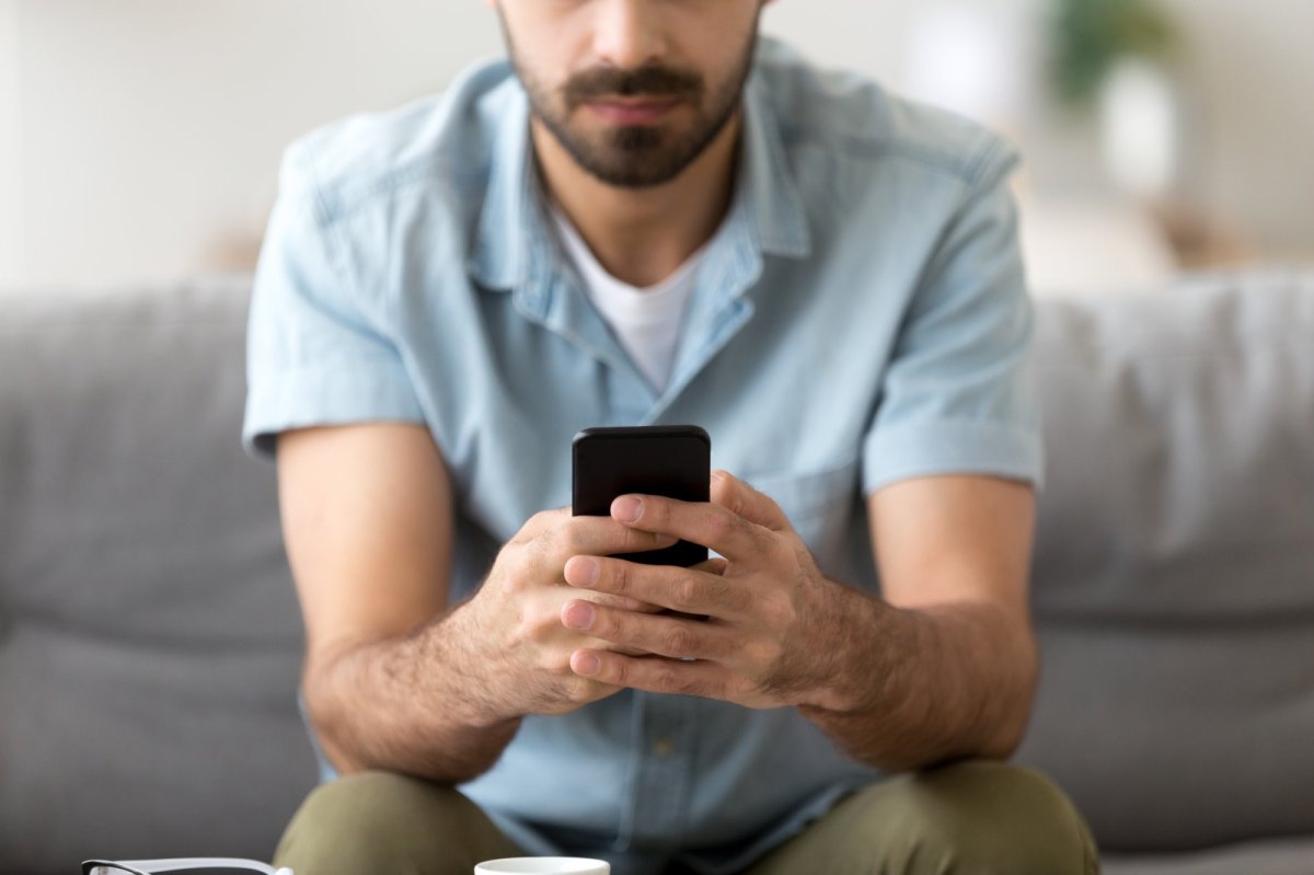 Mann mit Smartphone sitzt auf einem Sofa