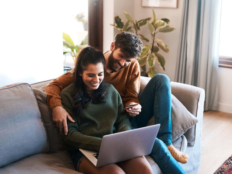 Mann und Frau sitzen mit dem PC auf dem Sofa.