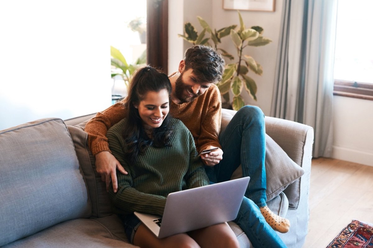 Mann und Frau sitzen mit dem PC auf dem Sofa.