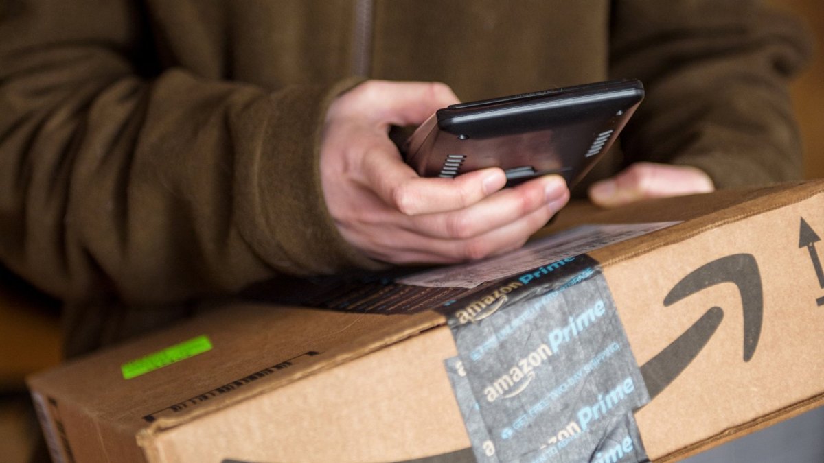 Jemand hält ein Amazon-Paket und sein Handy in der Hand.