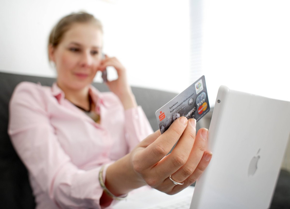 Eine Frau sitzt am Laptop und hält eine Sparkassen-Karte in der Hand.