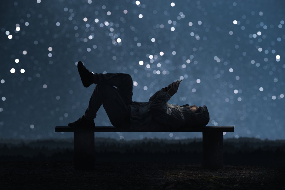 Mann liegt auf Bank mit Handy in der Hand vor Sternenhintergrund
