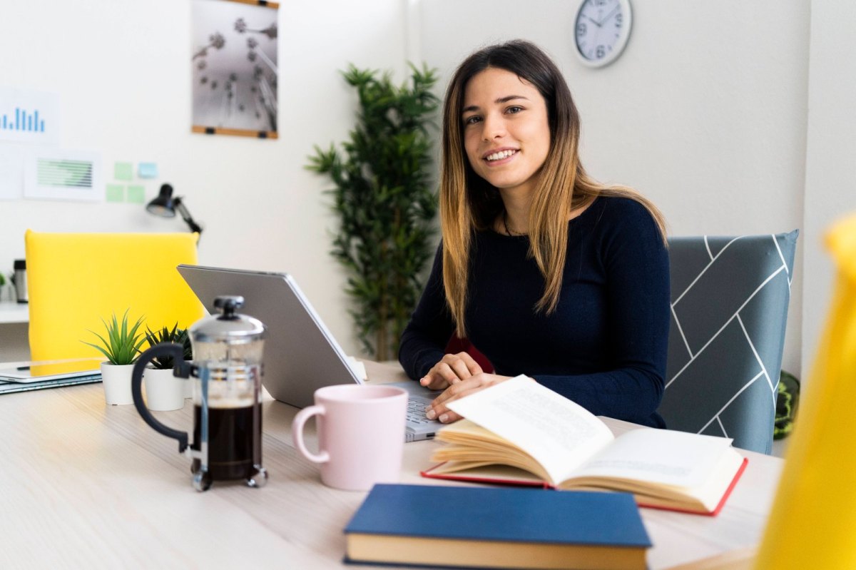 Junge Frau sitzt zu Hause an ihrem Schreibtisch und arbeitet am Laptop.