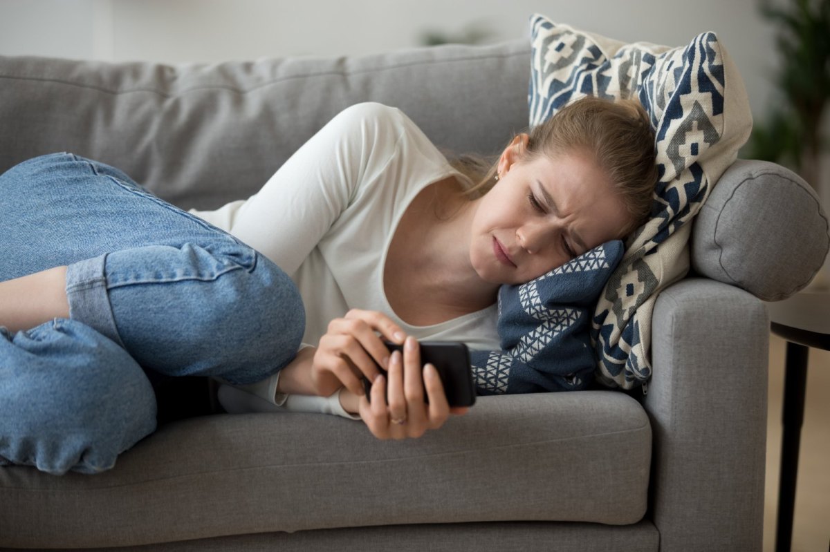 Frau liegt mit Handy traurig auf dem Sofa