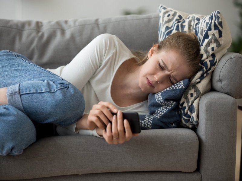 Frau liegt mit Handy traurig auf dem Sofa