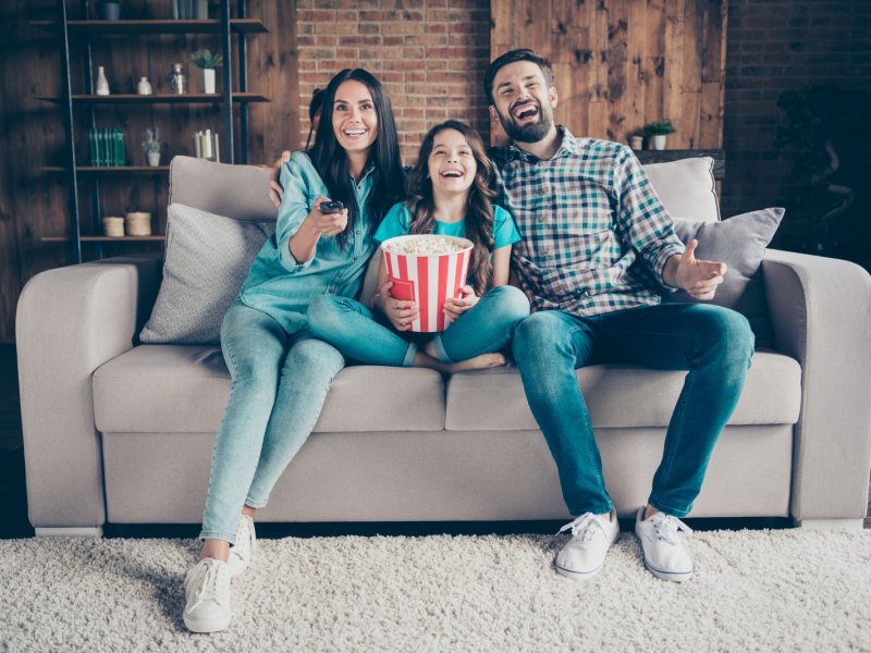 Familie sitzt mit Popcorn vor dem Fernseher.