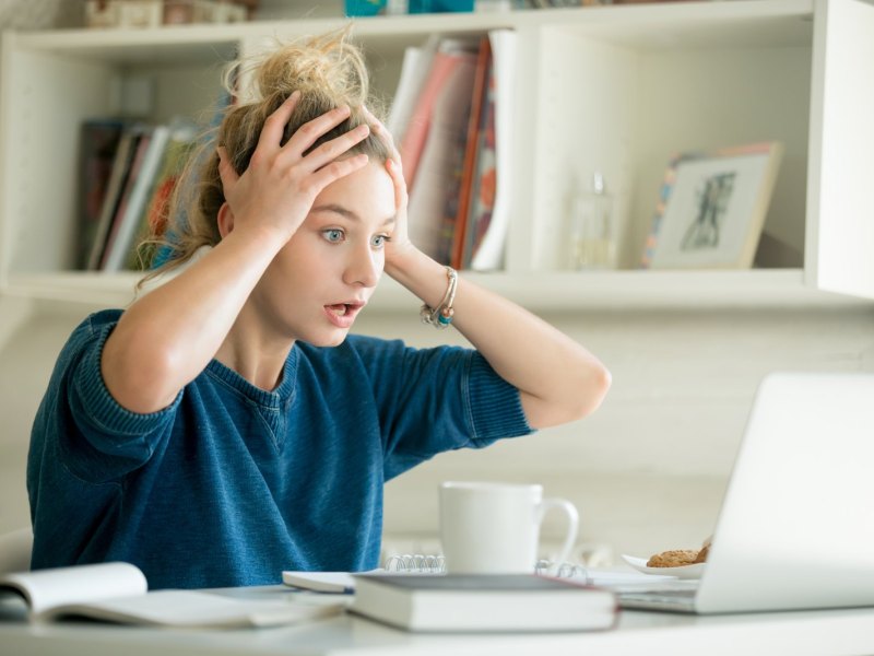 Frau fasst sich vor Schock an die Stirn und schaut auf ihren Computer.