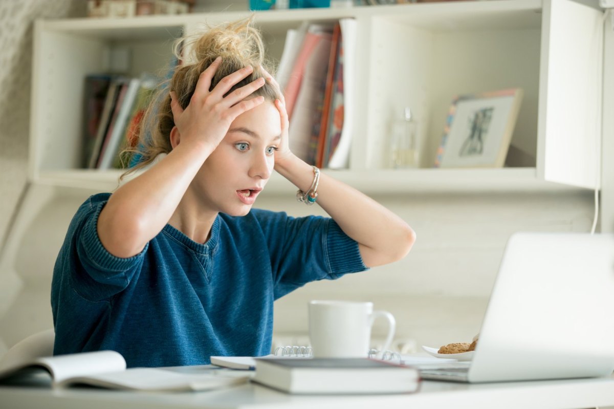 Frau fasst sich vor Schock an die Stirn und schaut auf ihren Computer.