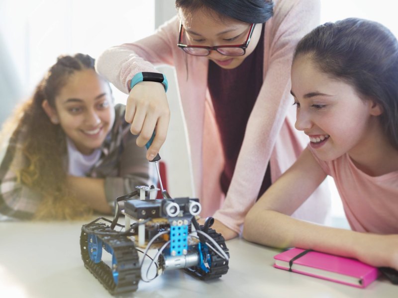 Schülerinnen untersuchen einen Miniroboter.