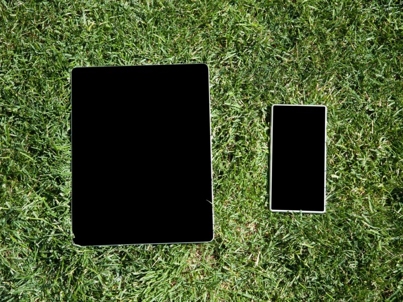 Smartphone und Tablet liegen auf Rasen